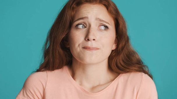 Upset worried redhead girl guiltily looking away over colorful background - 写真・画像