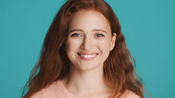 Pretty cheerful redhead girl happily looking in camera and smiling over colorful background - Φωτογραφία, εικόνα
