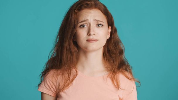 Upset redhead girl guiltily looking in camera over colorful background - 写真・画像