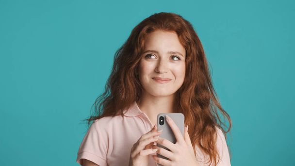 Beautiful charming redhead girl happily chatting on smartphone and smiling over colorful background - Фото, изображение