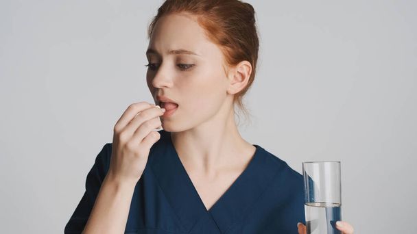 Portret van aantrekkelijke vrouwelijke arts het nemen van medische pillen en het drinken van zuiver water over witte achtergrond - Foto, afbeelding
