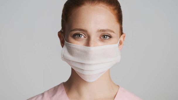 Retrato de una joven doctora con máscara médica mirando felizmente en cámara sobre fondo blanco. Concepto de seguridad - Foto, imagen