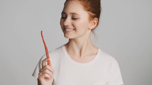 Kaunis hymyilevä tyttö onnellisesti poseeraa kameran kanssa hammasharja valkoisella taustalla - Valokuva, kuva