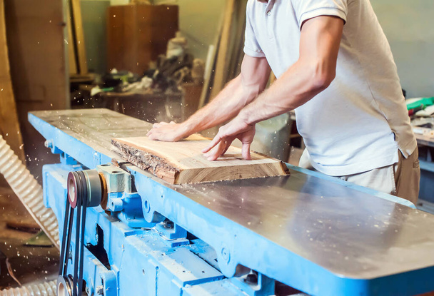 Um homem planeja uma prancha em um grande jointer industrial em uma oficina de carpintaria - Foto, Imagem