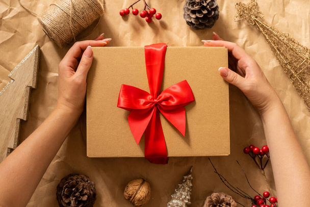 Weibliche Hände halten Geschenkbox auf Bastelpapier Hintergrund. Winterliche Festkomposition mit weihnachtlicher Stimmung. - Foto, Bild