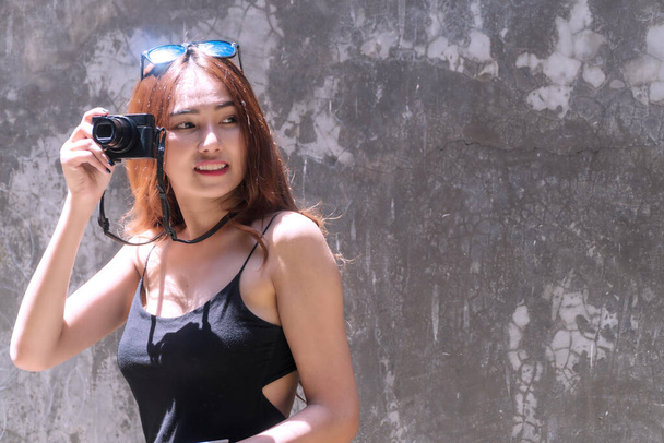 Веселая фотограф молодая женщина в солнцезащитных очках держит фотоаппарат, снимающий в городе. Путешественница молодая девушка использовать цифровую камеру сделать фото рефлекторное здание во время путешествия. Концепция фотографии. - Фото, изображение