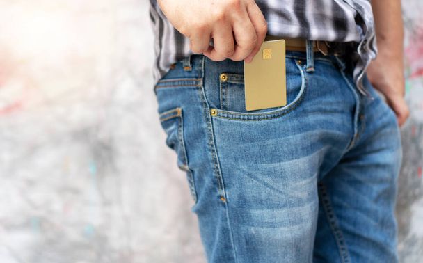 Manos de hombre joven recoger oro vacío tarjeta de crédito genérica de bolsillo vaqueros. Concepto de pérdida de dinero, negocios y finanzas. - Foto, imagen