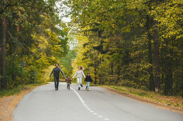 Happy family - mom, dad, son and daughter, are running. Parents and two children are running on the autumn road. They are having rest and enjoying beautiful autumn day. - Photo, Image
