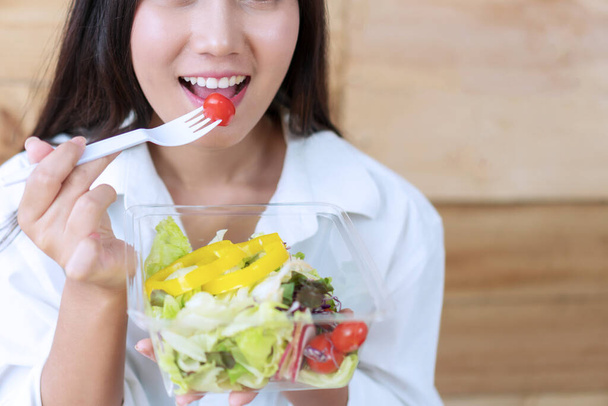 Gezond voedsel concept. Aantrekkelijke jonge vrouw ontbijten met salade vegetariër. Glimlachend meisje eet verse salade voor de gezondheid. - Foto, afbeelding