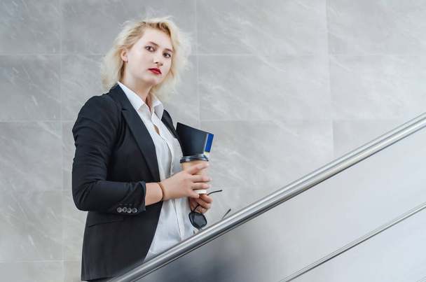femme blonde en costume d'affaires avec un dossier dans ses mains monte les escaliers. - Photo, image