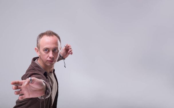 Adult man froze in a pose of martial arts. Confident glance wizard on a gray background. - Photo, Image