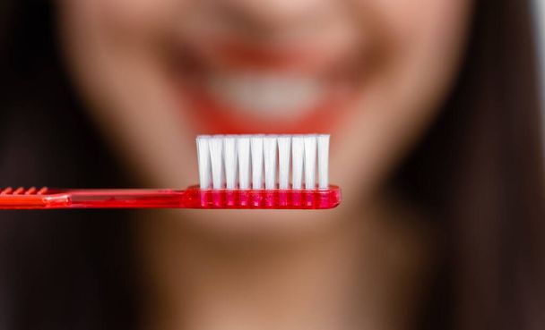 Smiling young woman with healthy teeth holds a toothbrush. Selective focus. Cropped photo. Blurred background. - Foto, Bild