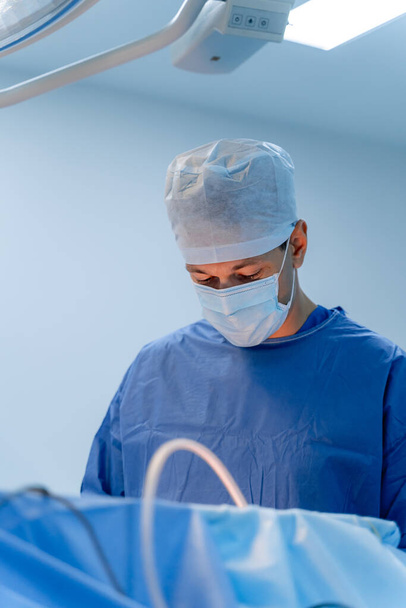 Portrait of a male doctor in scrubs. Male medic wears medical mask and hat. Selective focus on working process. - Fotografie, Obrázek