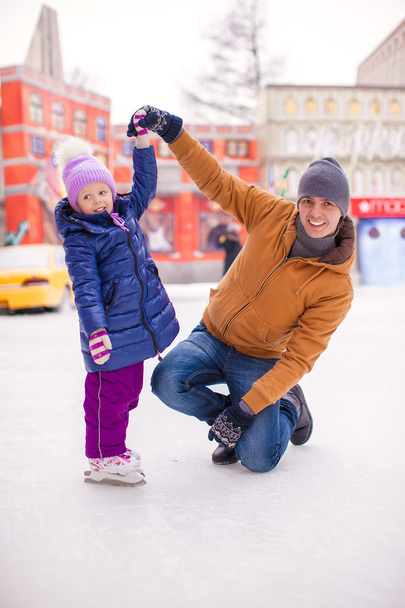 Молодий батько і чарівна маленька дівчинка розважаються на ковзанах
 - Фото, зображення