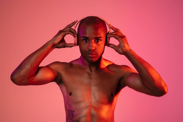 Image of african fitness man posing isolated over neon wall background while listening music with headphones - Fotó, kép