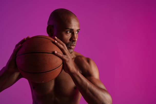 Image of athletic half-naked african american man playing basketball isolated over purple wall - Foto, immagini