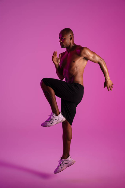 Photo of a handsome african fitness man isolated over pink wall background making sport exercises - Zdjęcie, obraz