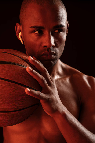 Image of african fitness man playing basketball isolated over black wall background while listening music with earphones - Photo, image