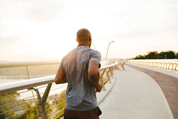 Вид збоку на молодого африканського чоловіка бігуна, який займається на відкритому повітрі на мосту
 - Фото, зображення