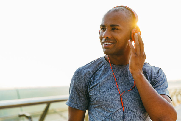 African american athlete man listening to the music outdoors, standing on a bridge - Fotó, kép