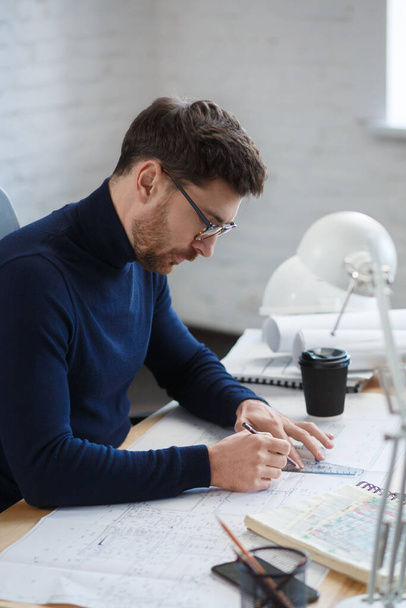 Architect working in office with blueprints.Engineer inspect architectural plan, sketching a construction project.Portrait of handsome bearded man sitting at workplace. Business construction concept - Φωτογραφία, εικόνα