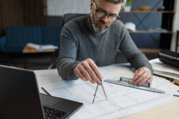 Interior designer working in office with blueprints.Engineer inspect architectural plan, sketching a construction project.Portrait of handsome bearded man at workplace. Business construction concept - Foto, imagen
