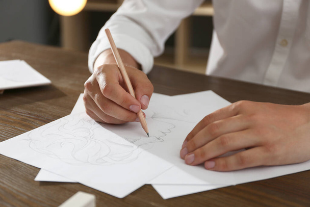 Mies piirustus muotokuva kynällä paperiarkille puupöydässä, lähikuva - Valokuva, kuva