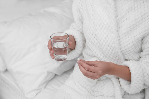 Young woman with glass of water taking pill in bedroom, closeup - Фото, зображення
