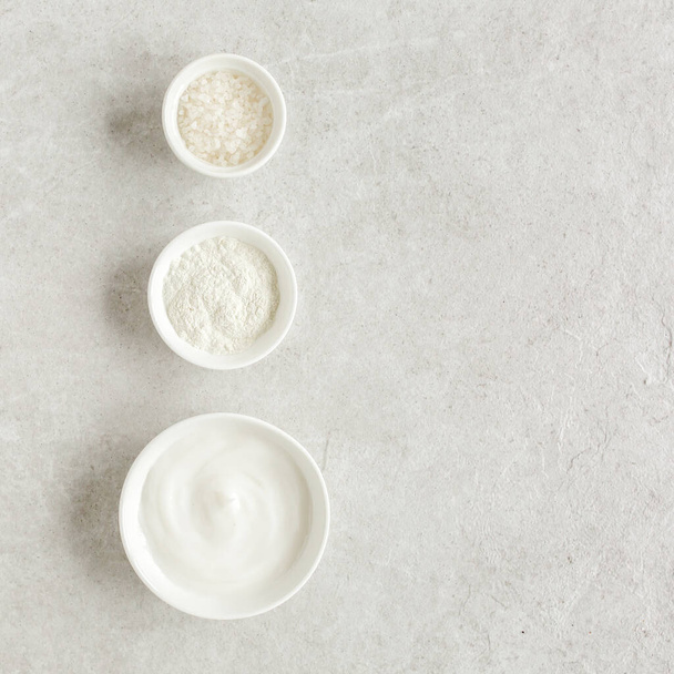 Three various natural spa cosmetics products in a bowl: facial cream, cosmetic clay, sea salt on gray marble background. Skincare concept.  - Zdjęcie, obraz