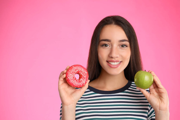 Woman choosing between apple and doughnut on pink background - Fotoğraf, Görsel