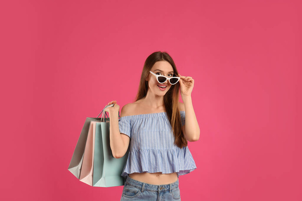 Beautiful young woman with paper shopping bags on pink background - Valokuva, kuva
