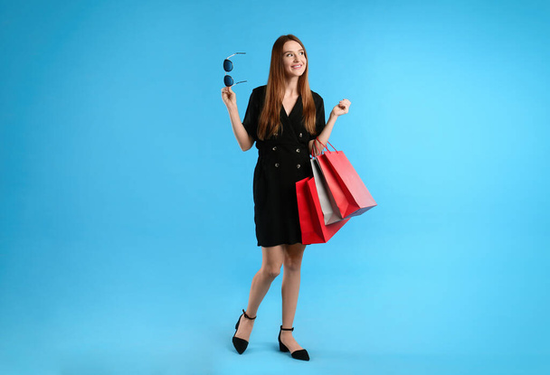 Beautiful young woman with paper shopping bags on light blue background - Foto, Imagem