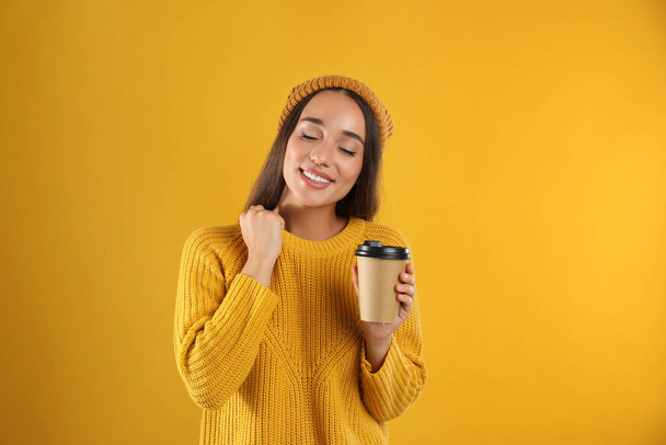 Happy beautiful woman with paper cup of mulled wine on yellow background - Foto, Bild