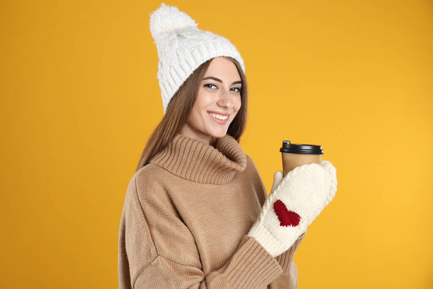 Happy beautiful woman with paper cup of mulled wine on yellow background - Foto, afbeelding