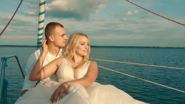 De bruid en bruidegom zitten op een jacht. Kijkend naar de verte bij zonsondergang. Prachtig landschap van wolken en meren - Video