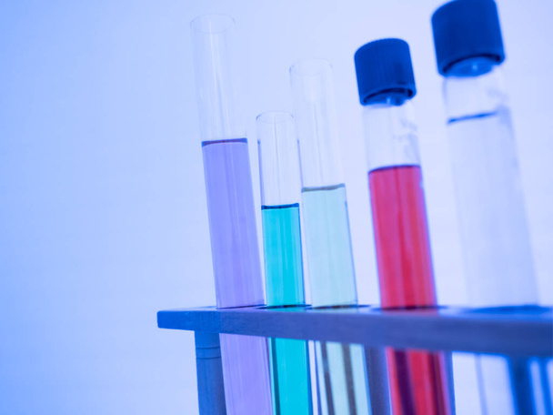 Im Reagenzglas befindet sich eine bunte Flüssigkeit. Stellen Sie auf einen Tisch für wissenschaftliche Experimente, Farbtöne. Nahaufnahme und selektive Fokussierung. - Foto, Bild