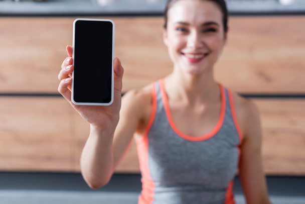Enfoque selectivo de la deportista mostrando teléfono inteligente con pantalla en blanco en casa  - Foto, Imagen