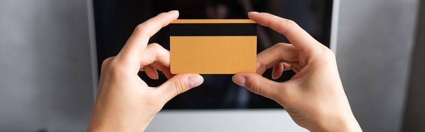 Image horizontale d'une femme tenant une carte de crédit près d'un écran d'ordinateur à la maison  - Photo, image