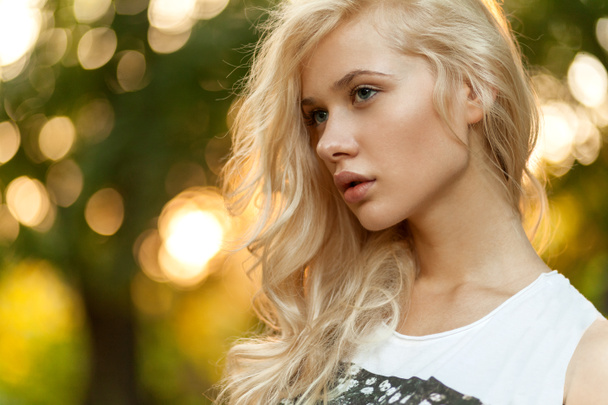 Nahaufnahme Porträt einer schönen blonden Frau mit lockigem blonden Haar mit gesunder Haut und Frisur weibliches Porträt natürliches Make-up, posiert im Park. - Foto, Bild