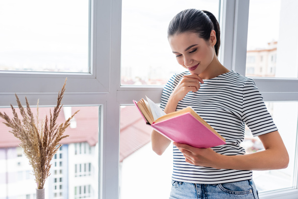 Giovane donna che legge libro vicino alla finestra a casa  - Foto, immagini