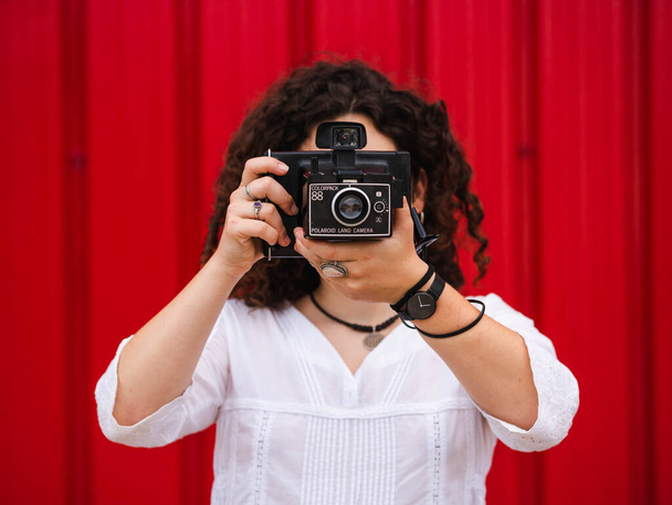Uma jovem fêmea atraente com uma antiga câmera fotográfica profissional contra um fundo vermelho - Foto, Imagem