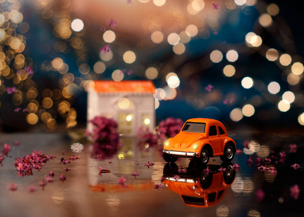 Juguete coche naranja en la superficie reflectante entre la decoración de primavera en el fondo de bokeh - Foto, Imagen