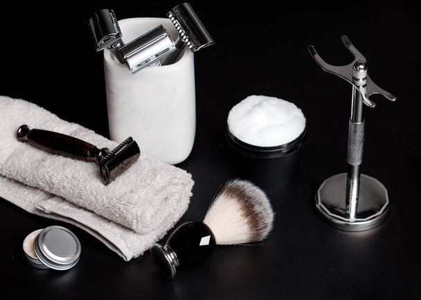 Rasoir et brosse sur pied, serviettes, parfum, baume et lames sur fond noir. - Photo, image