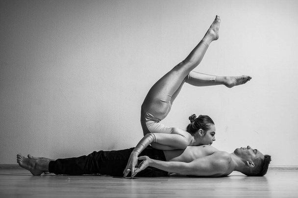 A duet of acrobats showing a pair trick. A woman in gymnastics overalls in a handstand over a shirtless man lies on his back. Very flexible circus performers. - Fotó, kép