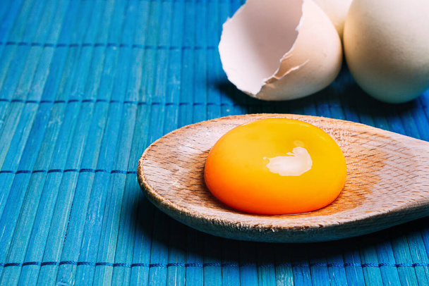 Yema de huevo cruda en una cuchara junto a los huevos, sobre un fondo azul Cocina ecológica, tradicional y saludable - Foto, Imagen