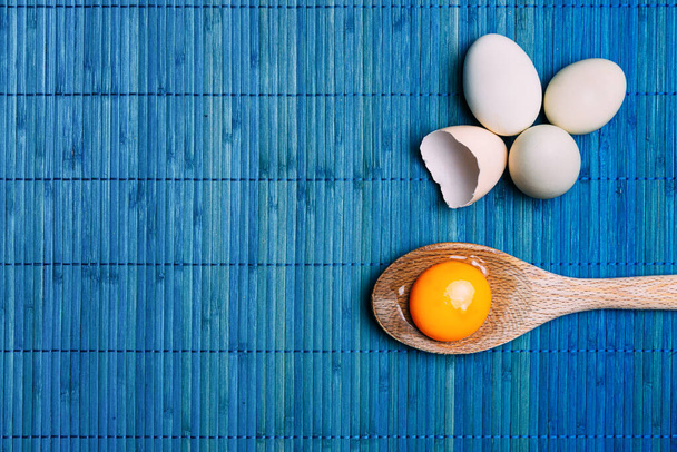 Rauwe eigeel in een lepel naast eieren, op een blauwe achtergrond Ecologisch, traditioneel en gezond koken - Foto, afbeelding