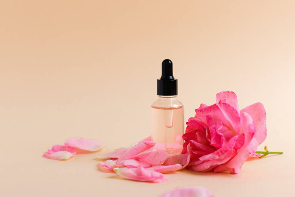 Eine Flasche mit Kollagen oder Hyaluronsäure auf neutralem Hintergrund mit einer Rosenblüte. Platz für Text. Kosmetik, Hautpflege, sanfte Pflege - Foto, Bild
