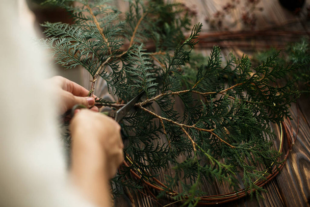 Making rustic christmas wreath. Hands holding green cedar branches on rustic wooden background. Seasonal holiday workshop online, making festive decorations at home - Foto, immagini