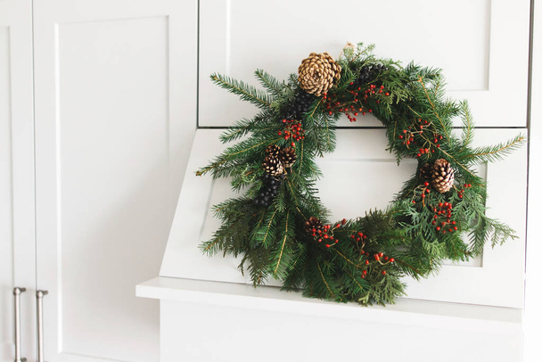 Kreativer moderner Weihnachtskranz, der an stilvollen Küchenschränken hängt. Rustikaler Adventskranz auf moderner Küchenhaube, festliche Weihnachtsdekoration. Frohe Weihnachten und frohe Feiertage - Foto, Bild