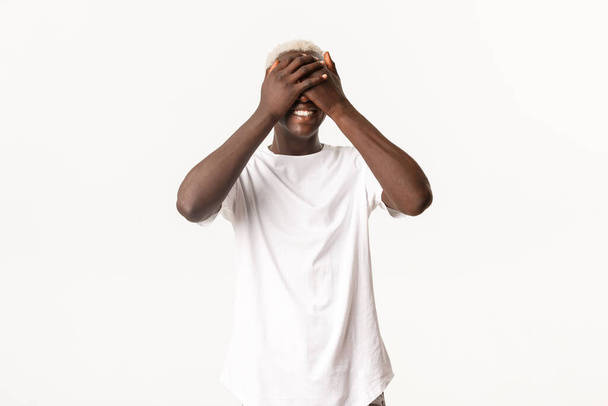 Портрет счастливого африканско-американского молодого парня, закрытые глаза и улыбающиеся, веселые, ожидая сюрприза, стоя на белом фоне - Фото, изображение